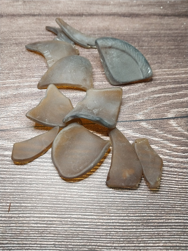 A close-up of hand tumbled sea glass in brown frosted dark amber colors, displayed on a wooden background.