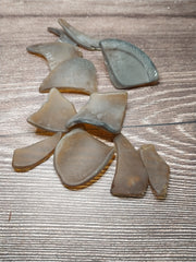 A close-up of hand tumbled sea glass in brown frosted dark amber colors, displayed on a wooden background.