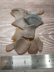 A close-up of assorted hand-tumbled brown frosted sea glass pieces arranged near a ruler.