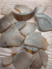 A collection of brown frosted sea glass pieces from vintage bottles, placed on a wood surface.