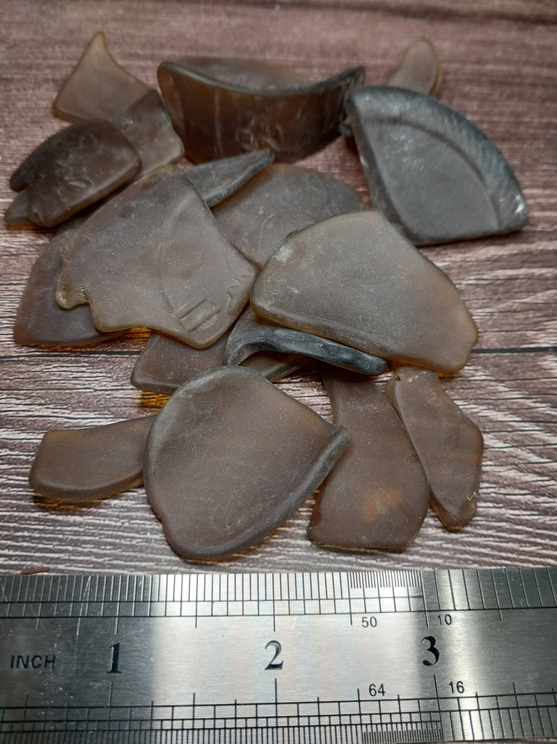 Brown frosted sea glass pieces placed next to a ruler to show size dimensions.