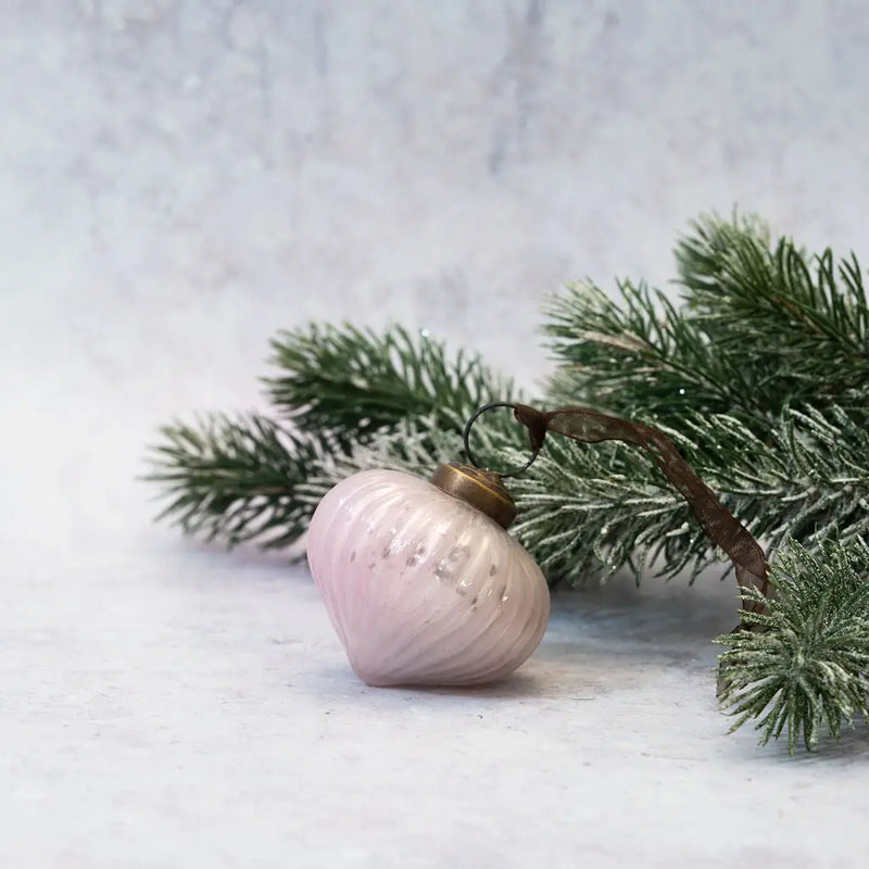 2" Alba Ribbed Lantern Glass Christmas Ornament in a soft pink hue with a bronze cap and brown organza ribbon, displayed next to a frosted pine branch on a neutral background.