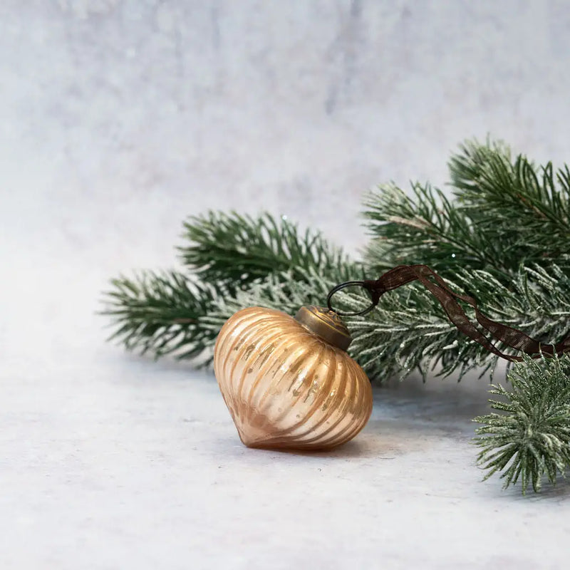 2" Champagne Ribbed Lantern Glass Christmas Ornament with a bronze cap and brown organza ribbon, displayed next to a frosted pine branch on a light background.