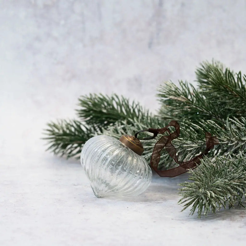 2" Clear Ribbed Lantern Glass Christmas Ornament with a bronze cap and organza ribbon, displayed next to a frosted pine branch on a neutral background.