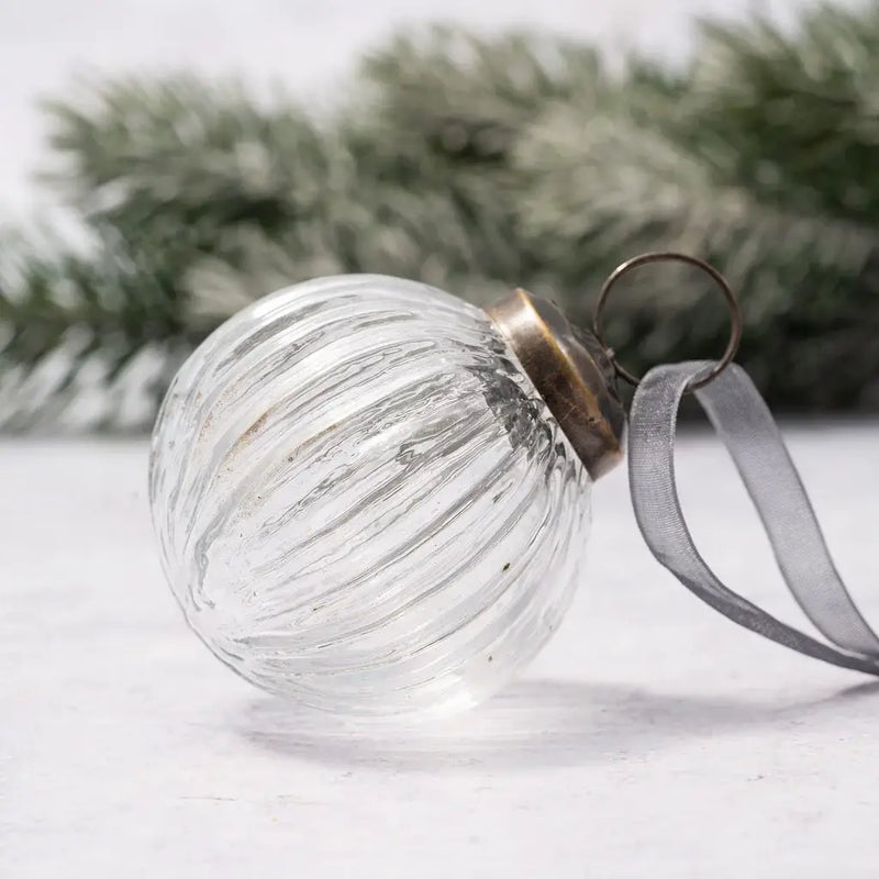 2" Clear Ribbed Round Christmas Tree Bauble with a bronze cap and grey organza ribbon, displayed next to a frosted pine branch on a neutral background.