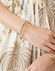 Woman wearing a gold toggle bracelet with a freshwater pearl charm, styled with another beaded bracelet, complementing a flowy patterned dress.