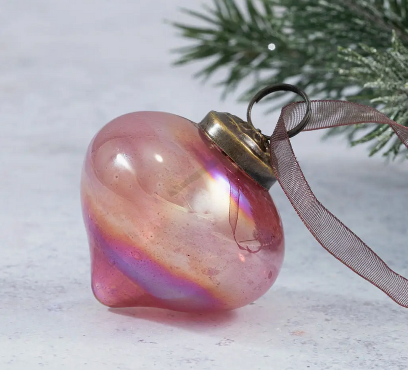 3" Mauve Luster Lantern Glass Ornament, semi-transparent with an iridescent finish and ornate bronze cap, lying on its side near frosted greenery.