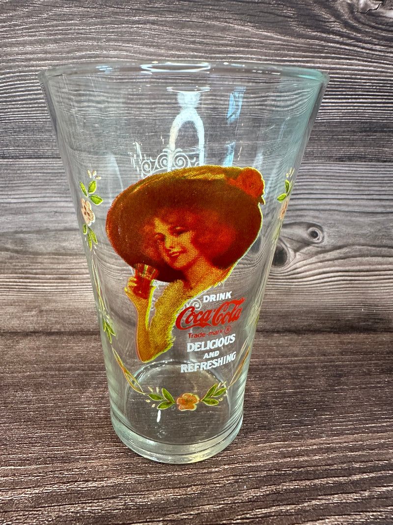 Vintage Coca Cola Magnificent Ladies Collector Series 1 Glasses featuring vibrant images of women in classic Coca-Cola advertising on a wooden surface.