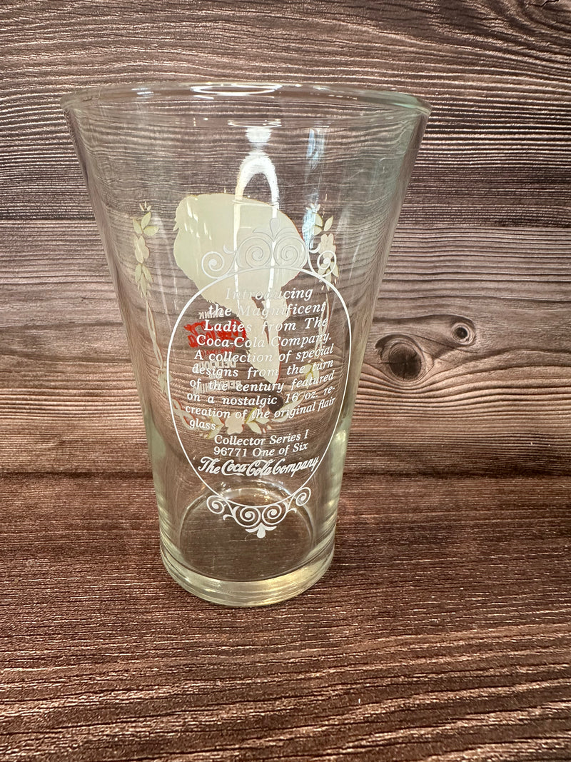 Vintage Coca Cola Magnificent Ladies Collector Series 1 Glasses featuring vibrant images of women in classic Coca-Cola advertising on a wooden surface.