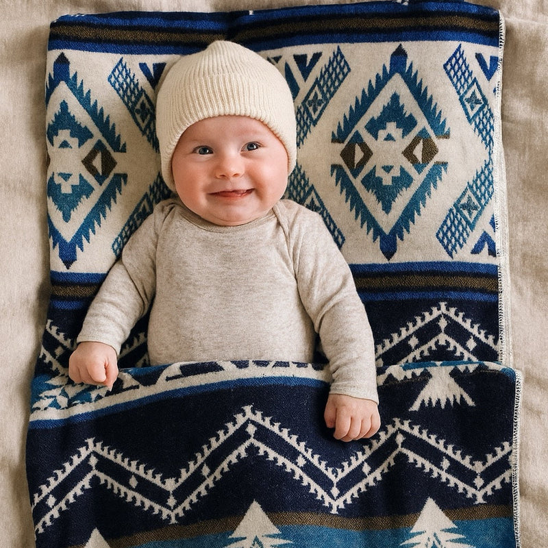 Adorable smiling baby resting on the Blue/Cream Luxury Alpaca Baby Blanket, soft and warm for newborns.