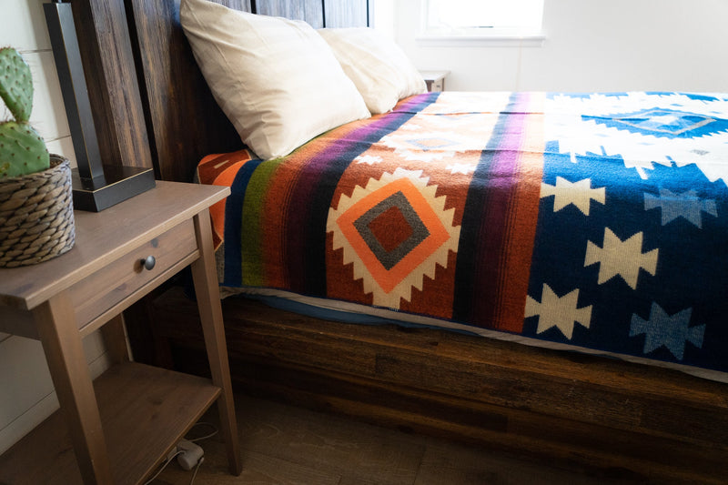 View of the Moab Alpaca Blanket on a bed next to a wooden bedside table, demonstrating its use as cozy bedding.