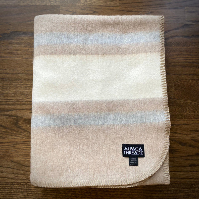 Tan and cream alpaca camp throw folded on wooden surface – soft neutral coastal home décor accent
