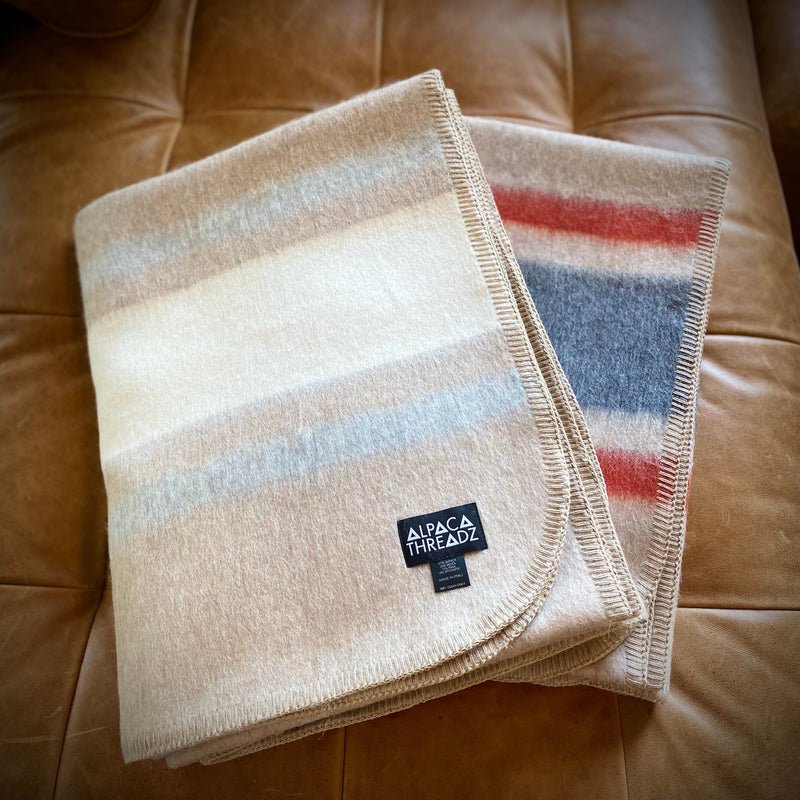 Tan cream and tan red alpaca camp throws folded together on leather sofa – premium coastal home décor accent