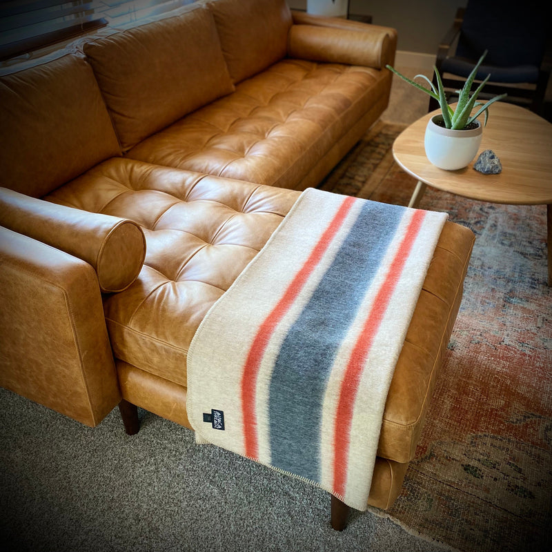 Tan and red alpaca camp throw draped over leather sectional sofa beside wooden table with plant – premium coastal living room décor accent