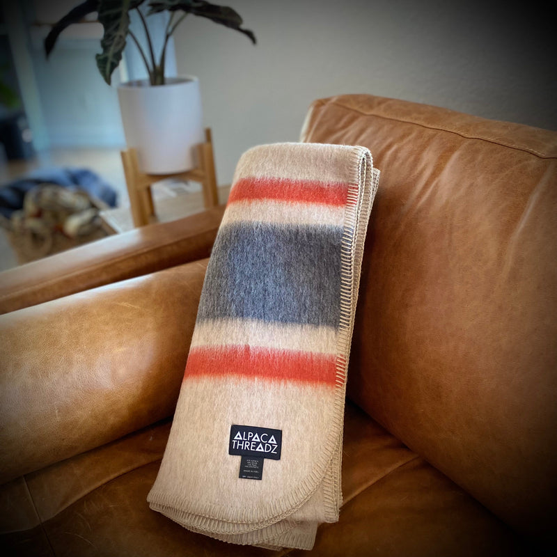 Tan and red alpaca camp throw draped over tan leather sofa – soft striped coastal home décor accent