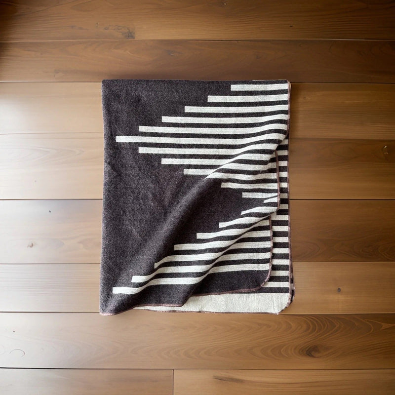 Overhead flat lay shot of the Coffee alpaca throw with zigzag and stripe patterns on a light wooden floor.