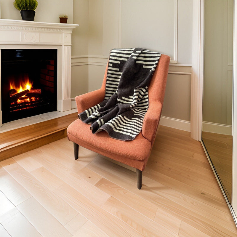 Coffee alpaca throw draped on a light pink armchair beside a fireplace, creating a cozy accent.