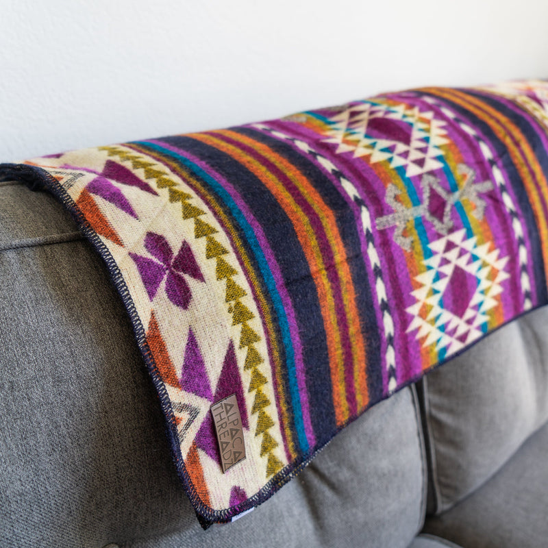 Amethyst alpaca blanket draped completely over the back of a gray sofa, showcasing the full geometric pattern and colors.