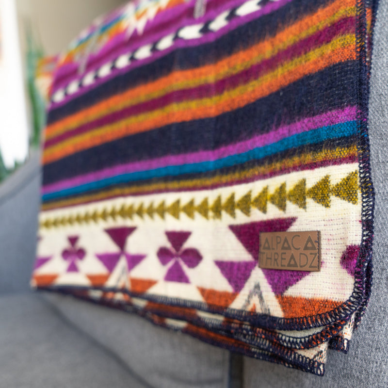 Close-up of the Amethyst alpaca blanket showing the dense purple, navy, and orange stripes and the cream geometric border.