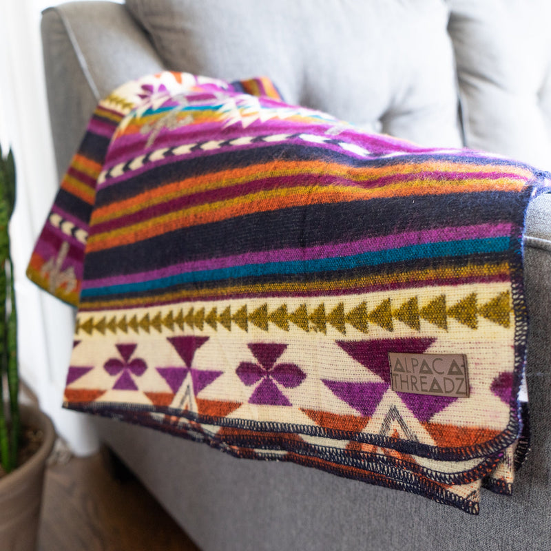 Side view of the Amethyst alpaca blanket draped over a gray sofa next to a snake plant, highlighting the reversible pattern.