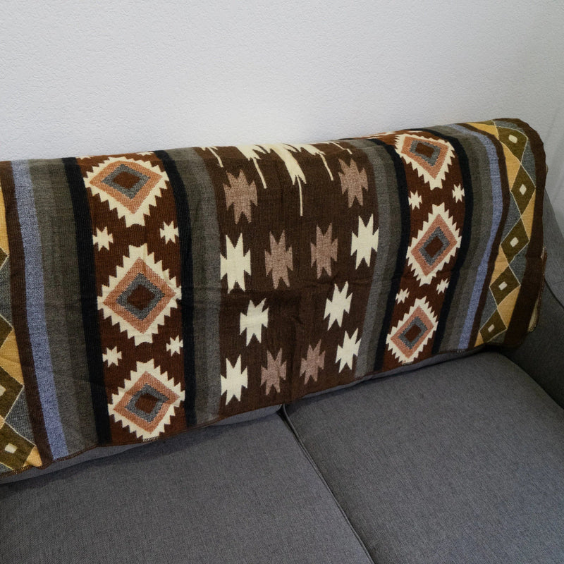 Andean Alpaca Wool Throw Blanket draped over the back of a gray sofa, showing the central pattern band featuring brown, gray, and white tribal motifs, including diamond and star geometric shapes.