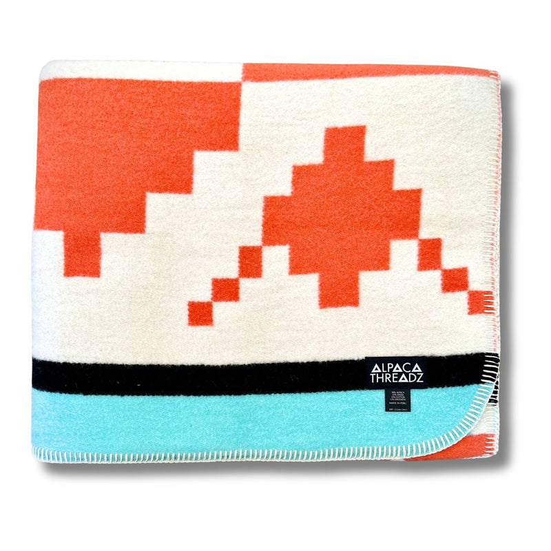 Folded corner view of the Aqua/White/Orange geometric alpaca blanket variant.