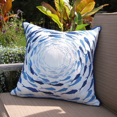 Azure Fish School Throw Pillow displayed on an outdoor patio chair, surrounded by greenery, emphasizing its suitability for outdoor use.