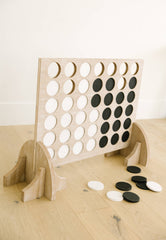 Wooden connect four game with black and white discs on a light wooden surface.