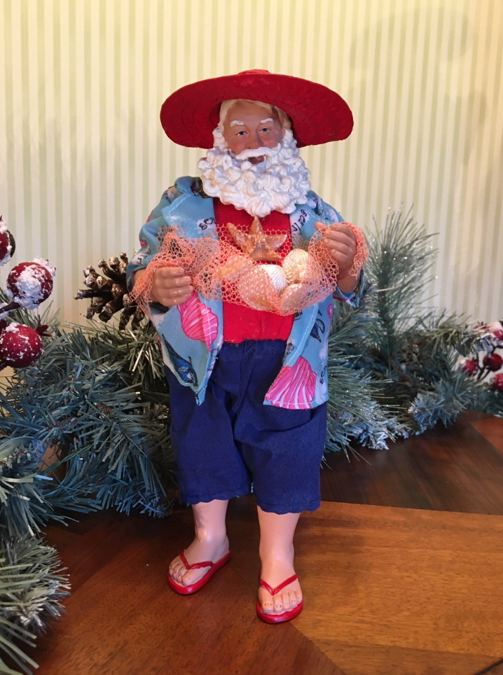 Beach Party Santa figurine surrounded by Christmas greenery and ornaments for festive coastal décor