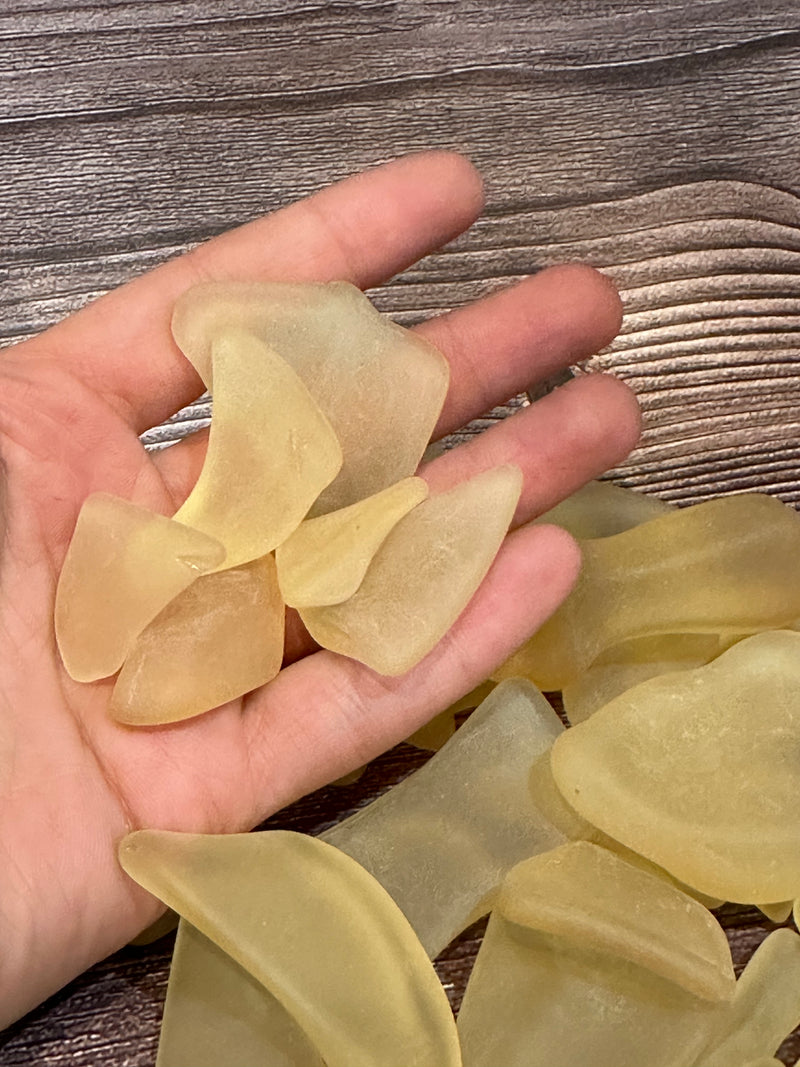 A hand holding yellow seaglass over a wooden background.