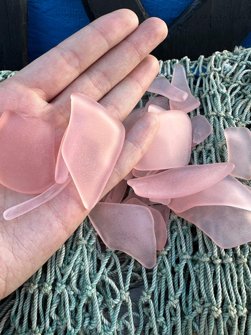 A hand holding pink sea glass over netting.