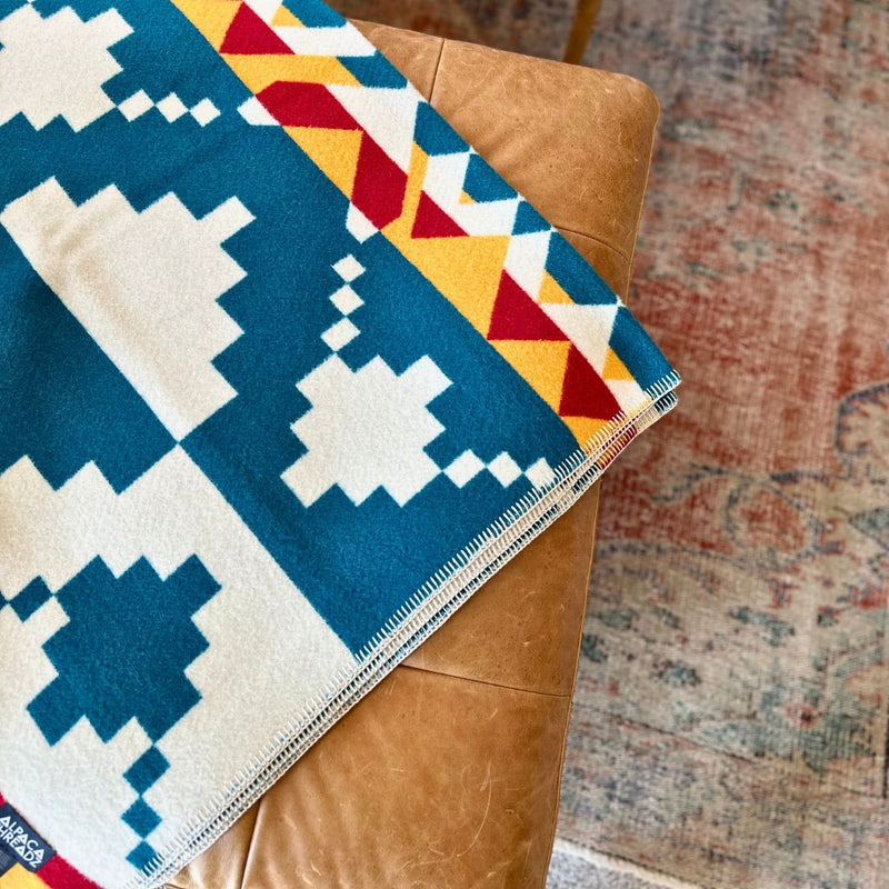 Top-down view highlighting the vibrant blue, yellow, and red geometric pattern of the alpaca throw on a chair or surface.