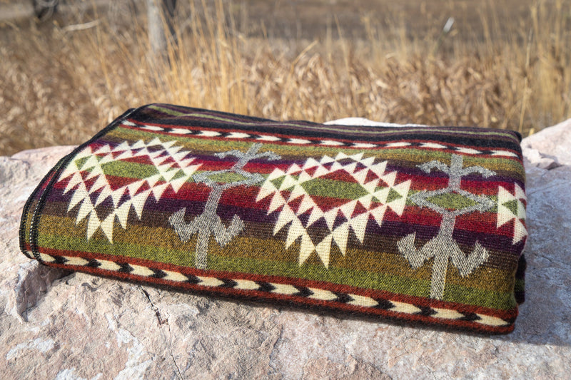 Close-up of the Cactus Alpaca Blanket draped over a rock, focusing on the horizontal stripes and geometric motifs.