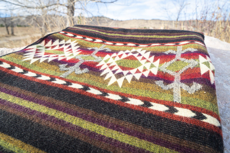 Overhead shot of the Cactus Alpaca Blanket on a rock, highlighting the woven texture and full pattern repeat of red, green, and cream.