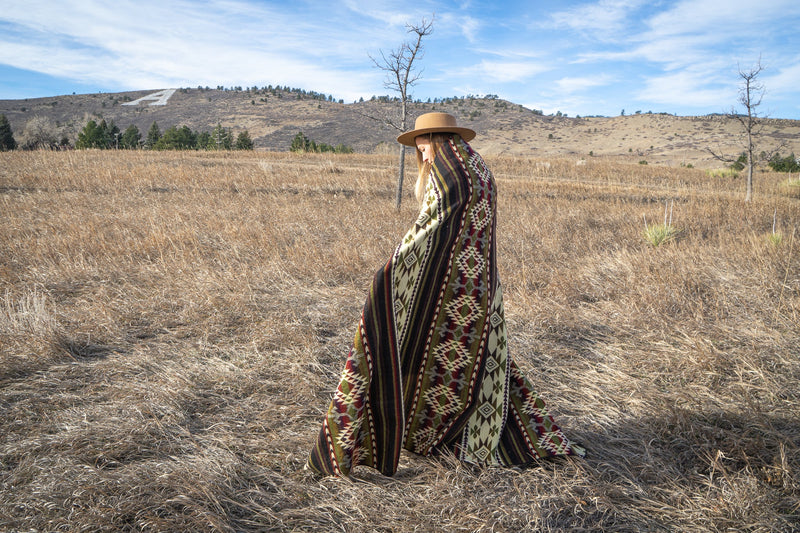 Woman holding the Cactus Alpaca Blanket completely spread out behind her, highlighting the full Queen size and pattern visibility.