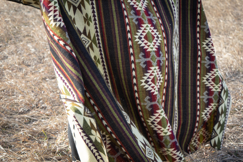 Woman completely wrapped in the Cactus Alpaca Blanket, standing tall in the grassy field.