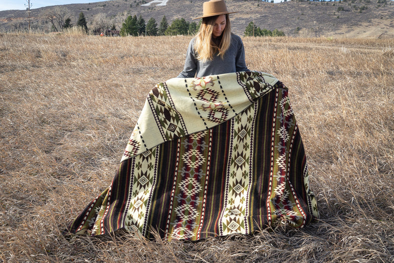 Woman wearing the Cactus Alpaca Blanket draped over her shoulder, seen in profile in the sunny, grassy field.