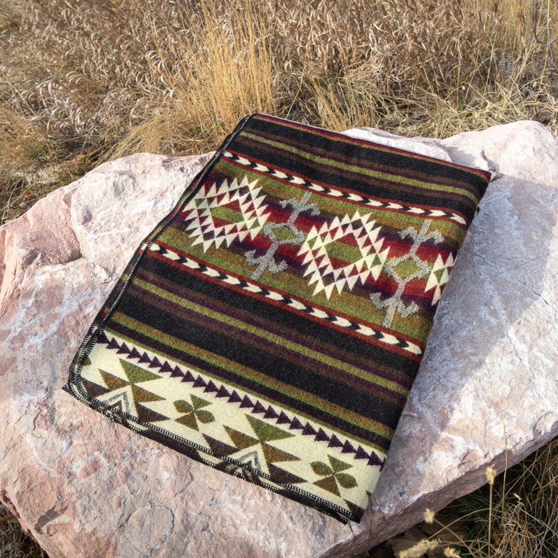 Cactus Alpaca Blanket neatly folded on a flat brown rock, showcasing the green and burgundy geometric pattern.