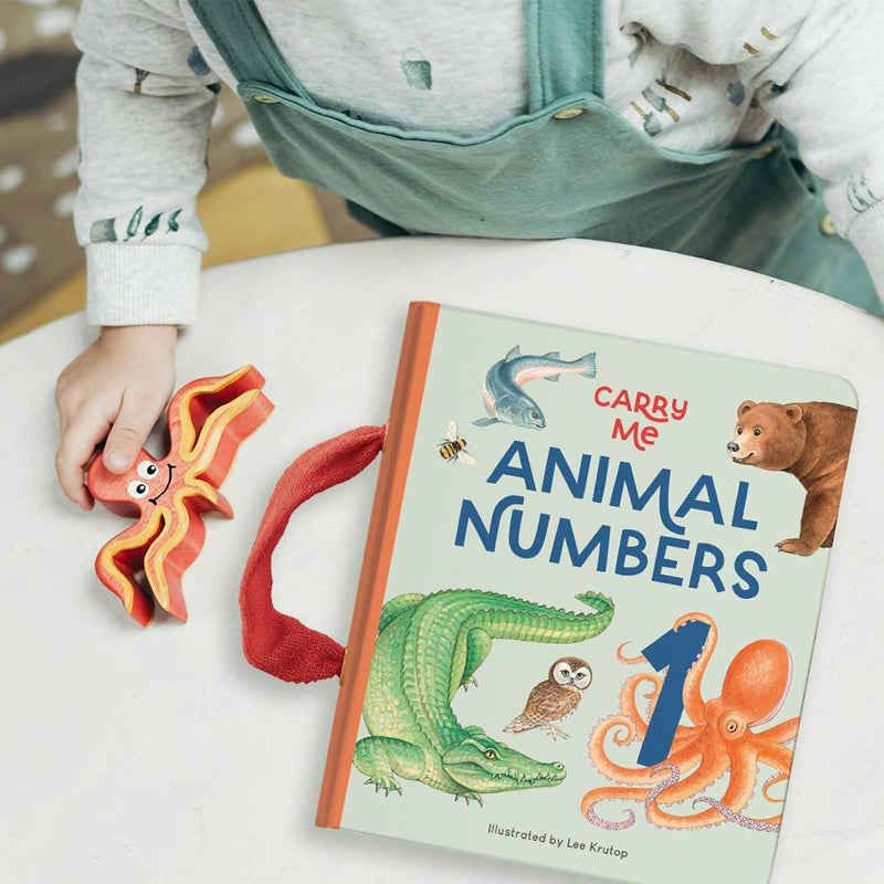 Child holding a toy next to a book titled 'Carry Me Animal Numbers' on a white surface.