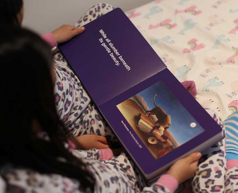 Children reading a book with a purple cover on a bed with a colorful pattern.