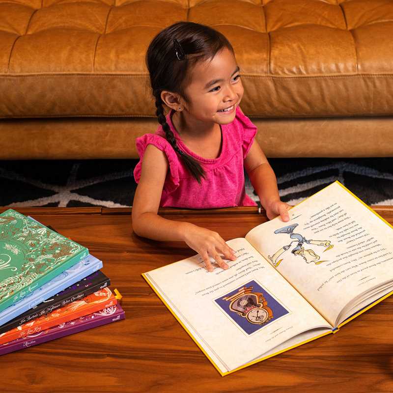 Young girl reading a book on a wooden floor with a brown couch in the background