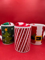 Group of festive Christmas mugs including tree, candy cane, and Santa designs displayed on red background.