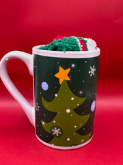Dark green mug decorated with Christmas trees and gold stars, paired with fuzzy socks.