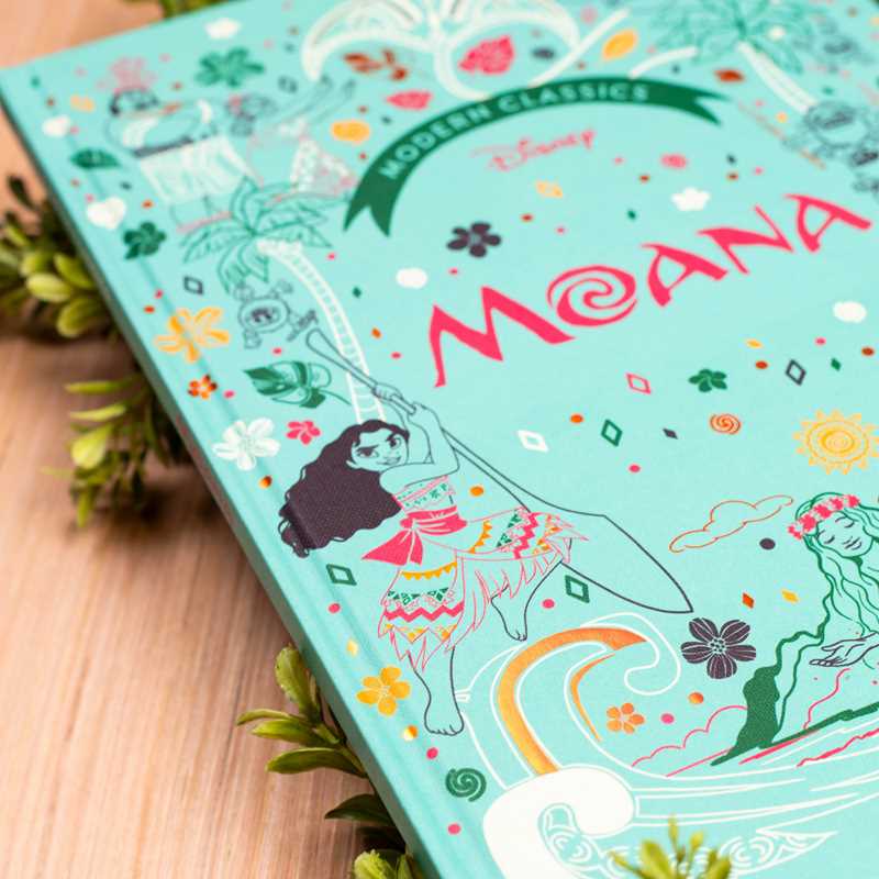 Colorful book cover of 'Moana' with illustrations and text on a wooden surface.
