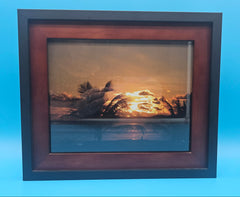 Framed coastal sunset photography print with palm silhouettes and warm orange glow – perfect for beach-inspired home décor.