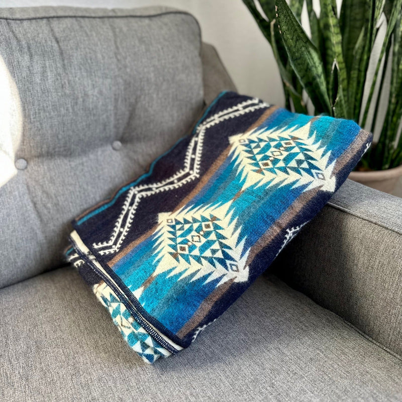 Cobalt Blue Alpaca Blanket folded into a clean rectangle and resting on a gray sofa, highlighting the blue, white, and geometric pattern.
