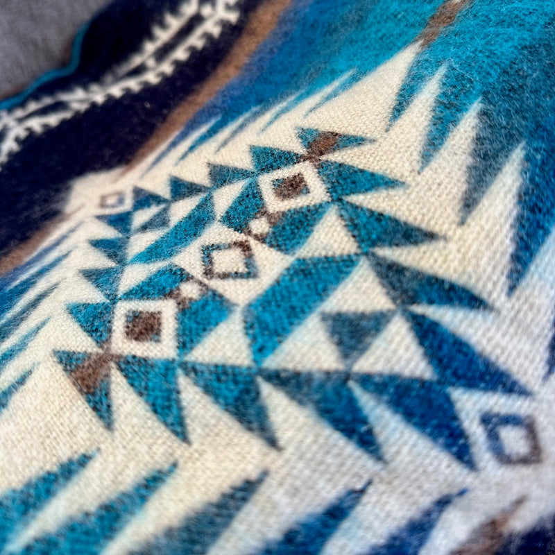 Extreme close-up of the Cobalt Blue blanket's geometric pattern, focusing on the interwoven light blue, dark blue, and small brown triangle motifs.