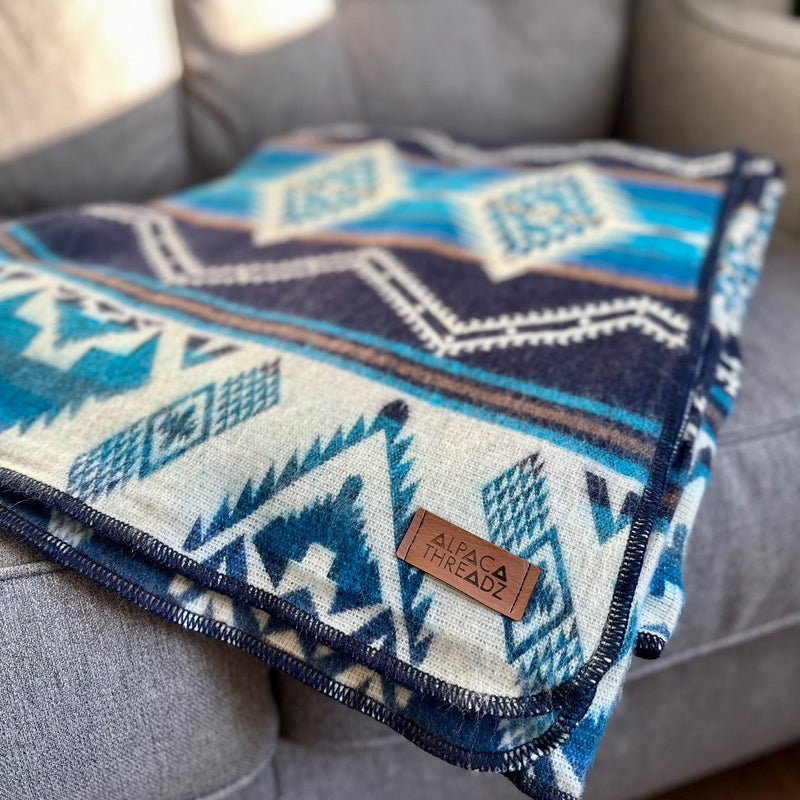Cobalt Blue Alpaca Throw angled and folded on the back of a gray sofa, showcasing the vibrant geometric design and depth of color.