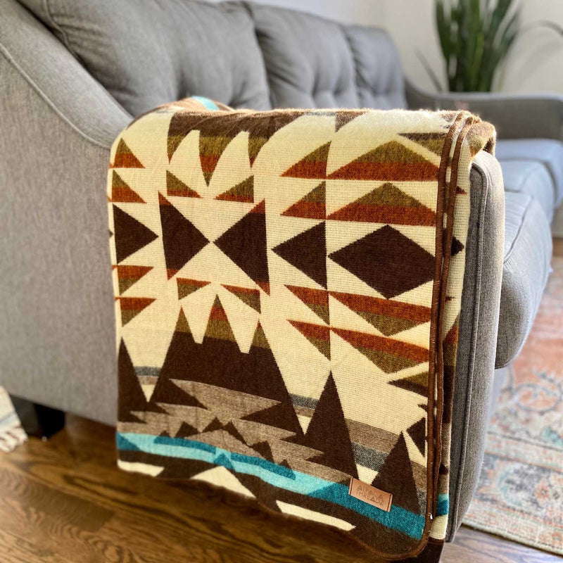 Wider shot of the Cowboy Andean Alpaca Blanket draped over a couch, highlighting the turquoise band and the Western-inspired geometric design.