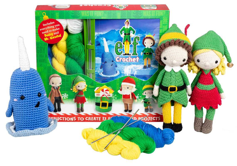 Crochet kit with elf dolls, blue narwhal, and yarn in front of 'Elf' movie poster packaging.